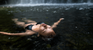 Woman floating in a small lake under a waterfall in Wales